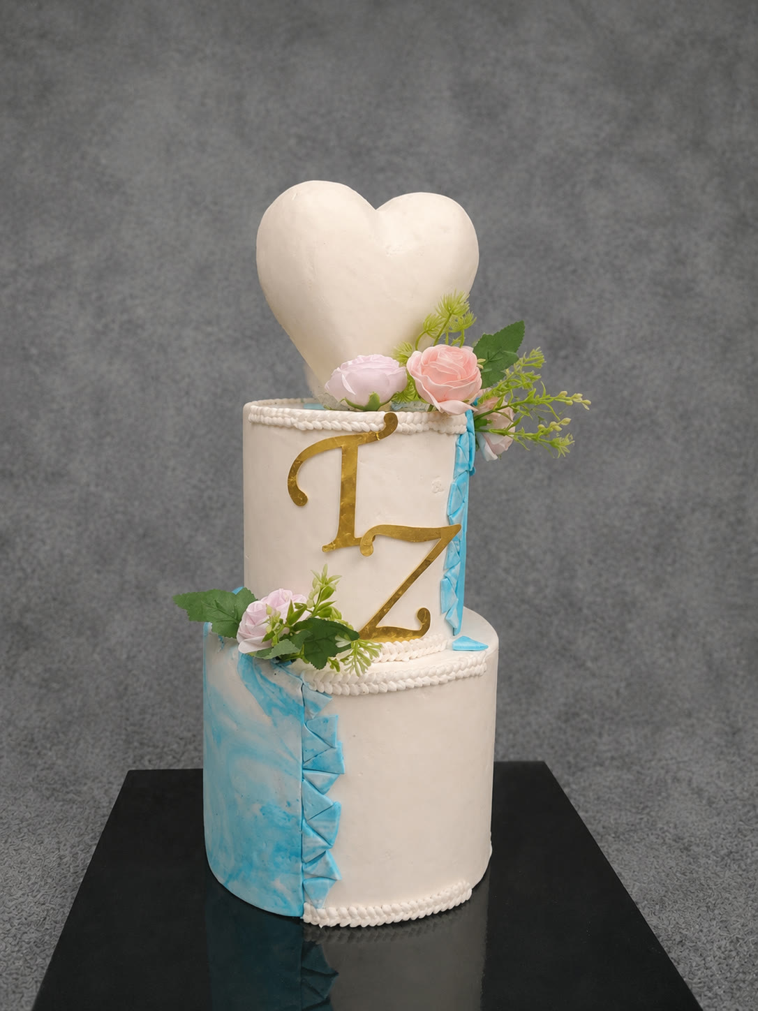 White three-tier wedding cake with a heart topper, gold initials and flowers